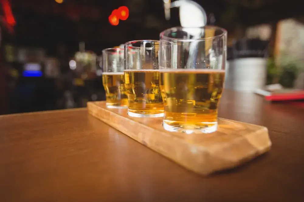 吧檯木盤上的品飲組合並排三杯金黃啤酒，一次比較黃金艾爾與其他風格最省成本