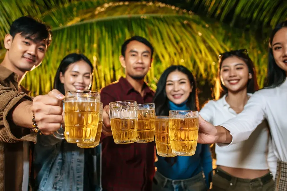 三五好友在戶外烤肉舉杯，桌上擺著金黃與琥珀色的啤酒